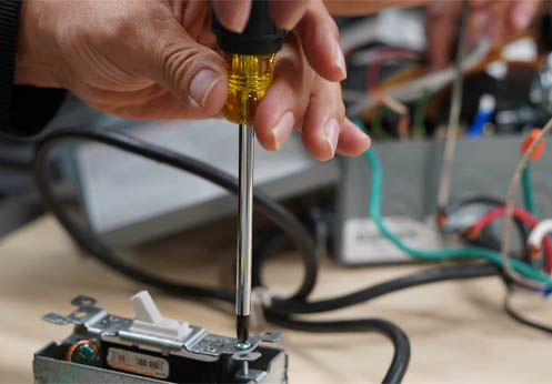 A student using a screwdriver to secure a light switch.