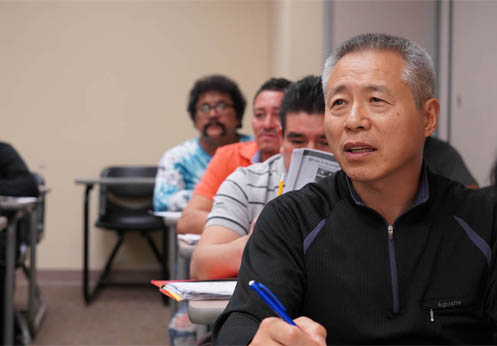 A row of ESL students taking notes in class.