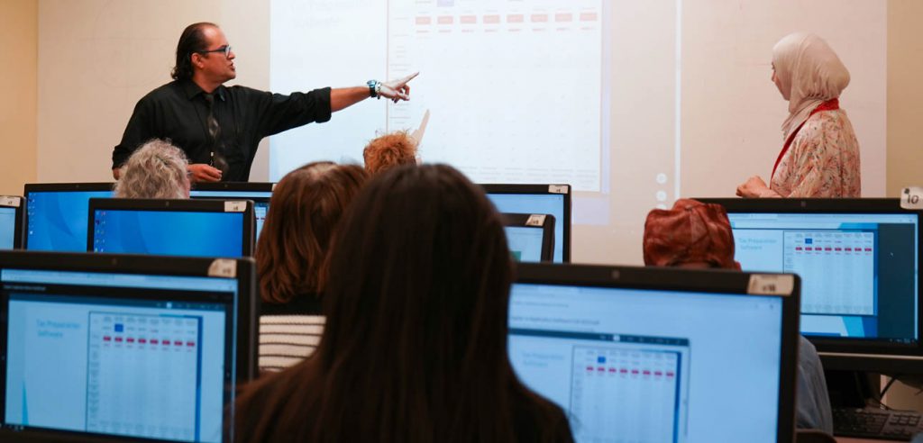 A photo of the computer class for the Administrative professional certificate. The instructor speaking towards the students.