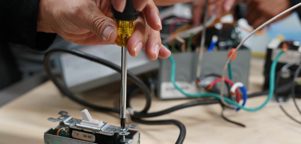 An electrical technology class photo. A student using a screwdriver to secure a light switch.