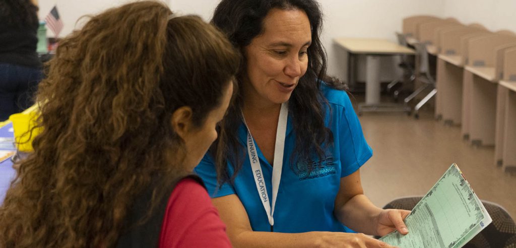 A photo of a NOCE counselor helping a student navigate through the listed resource on an event flier.