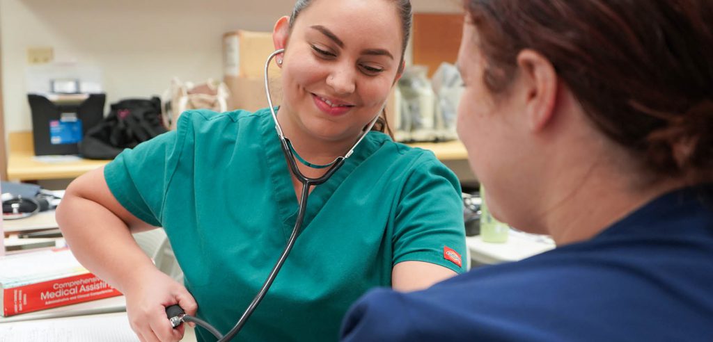 A photo of a medical assistant student practicing taking blood pressure on another student.