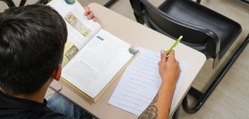 Adult student reading a textbook and taking notes to prepare for their GED exam.