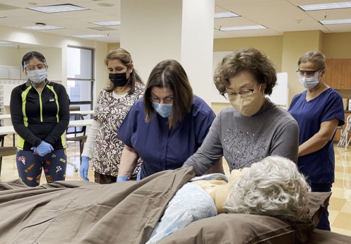 Personal care aide students learning how to move a patient in bed.