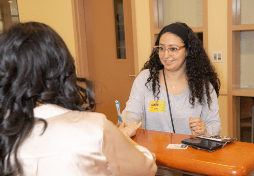 A female student with glasses and dark brown curly hair getting registration assistance at the Anaheim Admissions and Records desk.