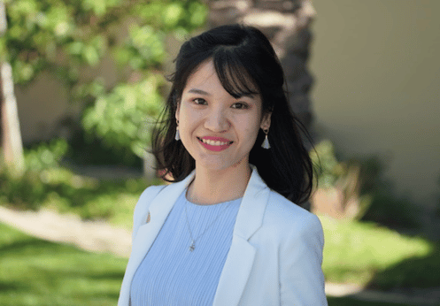 An Asian woman smiling in a white blazer and light blue blouse.