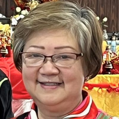 Marijo Prey wearing glasses and red attire at a formal event with decorative background.